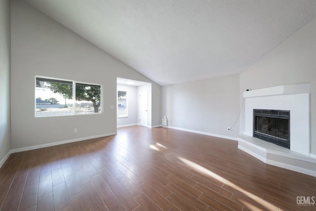 unfurnished living room with dark wood-style flooring, baseboards, vaulted ceiling, a textured ceiling, and a fireplace with raised hearth
