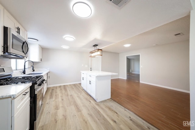 kitchen featuring baseboards, light wood-style flooring, visible vents, appliances with stainless steel finishes, and a sink