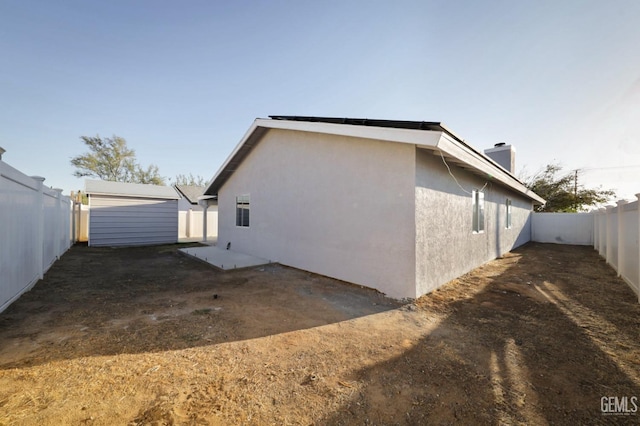 view of property exterior with a fenced backyard, an outdoor structure, stucco siding, and a chimney