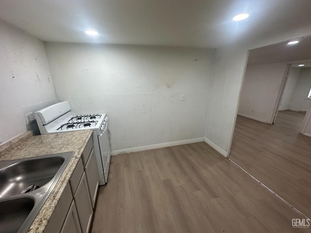 kitchen featuring light wood finished floors, baseboards, white gas range, light countertops, and a sink