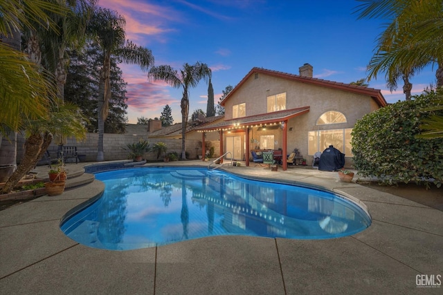 pool at dusk featuring a grill and a patio