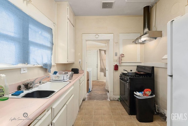 kitchen with visible vents, black gas range oven, freestanding refrigerator, a sink, and wall chimney range hood