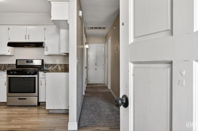 1929 Belmont St, Delano, CA 93215 - kitchen featuring stainless steel range with gas cooktop, under cabinet range hood, dark countertops, white cabinetry, and a textured ceiling