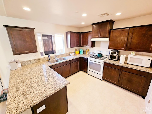 kitchen featuring light stone countertops, white appliances, dark brown cabinetry, sink, and kitchen peninsula