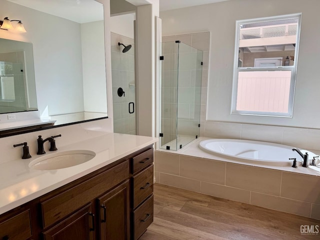 bathroom featuring wood finished floors, a stall shower, a garden tub, and vanity