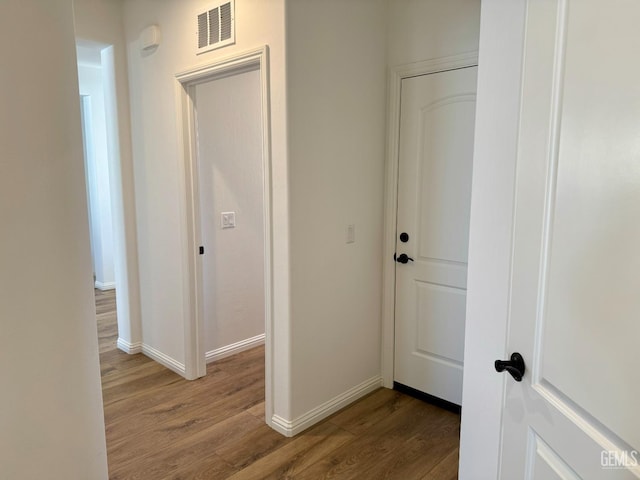 hall featuring baseboards, visible vents, and wood finished floors