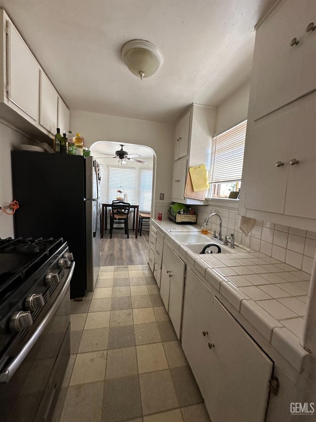 kitchen featuring plenty of natural light, high end stainless steel range oven, sink, white cabinets, and tile counters