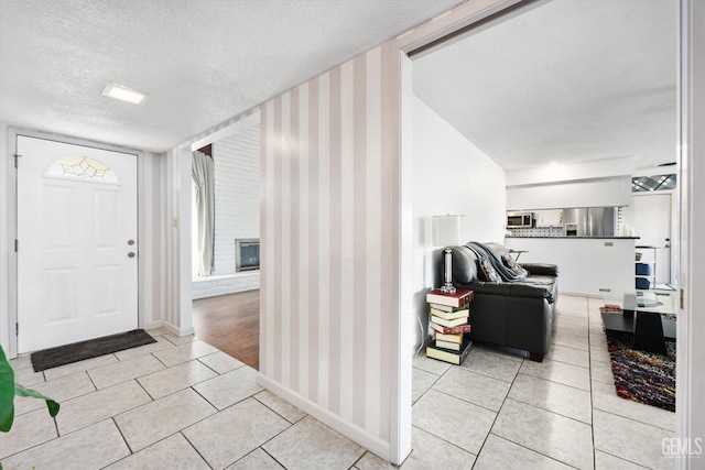 foyer featuring a textured ceiling, light tile patterned flooring, and a brick fireplace