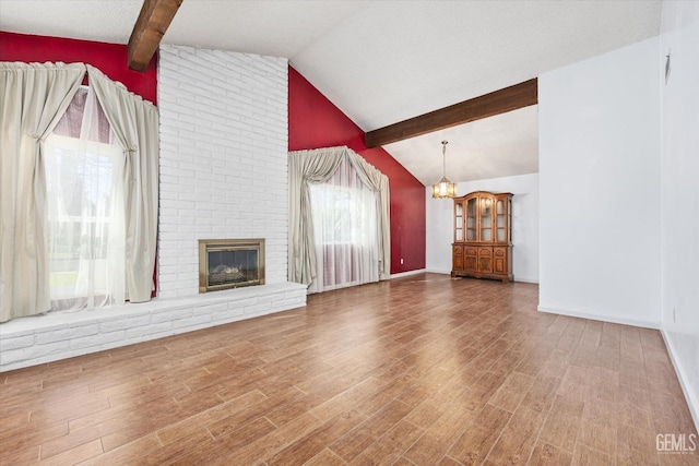 unfurnished living room featuring lofted ceiling with beams, a brick fireplace, a notable chandelier, and wood finished floors