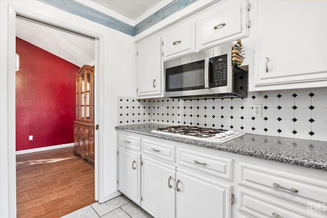 kitchen with tasteful backsplash, stainless steel microwave, white gas cooktop, and white cabinetry