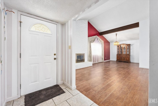 foyer entrance with a fireplace, lofted ceiling with beams, a textured ceiling, wood finished floors, and a chandelier