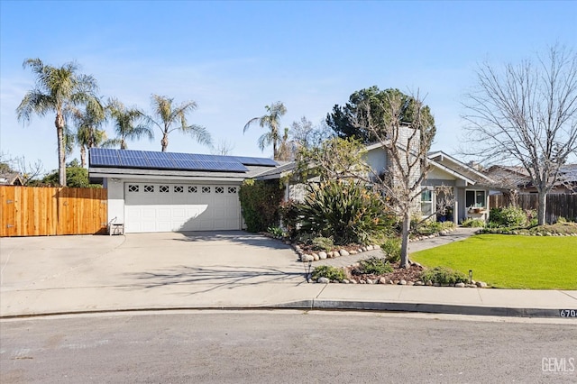 view of front of home featuring an attached garage, fence, driveway, roof mounted solar panels, and a front lawn