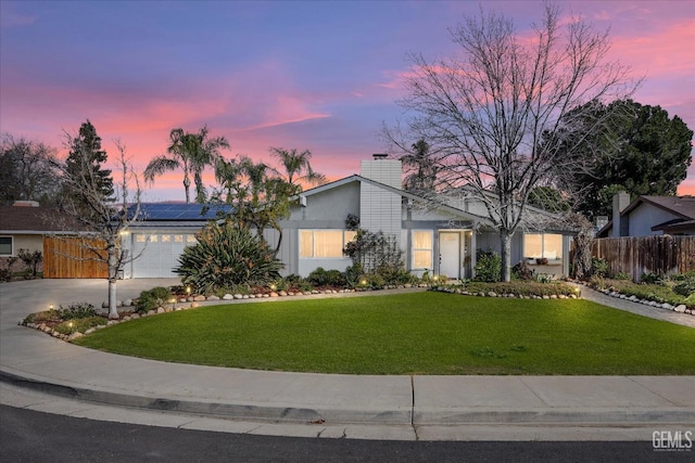 mid-century home with a yard, concrete driveway, an attached garage, roof mounted solar panels, and fence