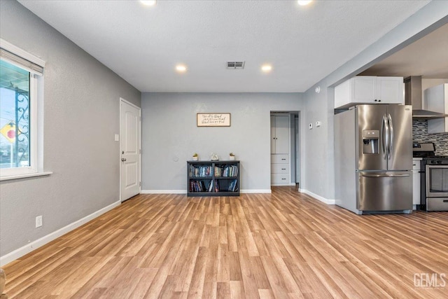 kitchen with white cabinetry, backsplash, wall chimney exhaust hood, stainless steel appliances, and light hardwood / wood-style flooring