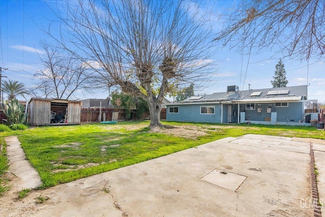 back of property featuring a storage unit, a patio area, a lawn, and solar panels