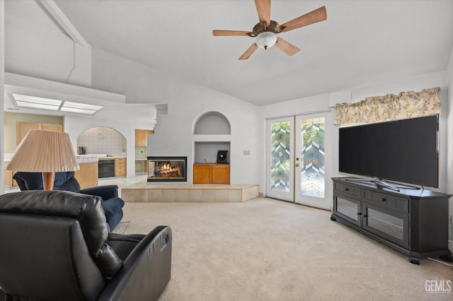 living room featuring built in shelves, ceiling fan, light colored carpet, vaulted ceiling, and a tiled fireplace