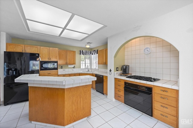 kitchen with tile countertops, a center island, black appliances, sink, and decorative backsplash