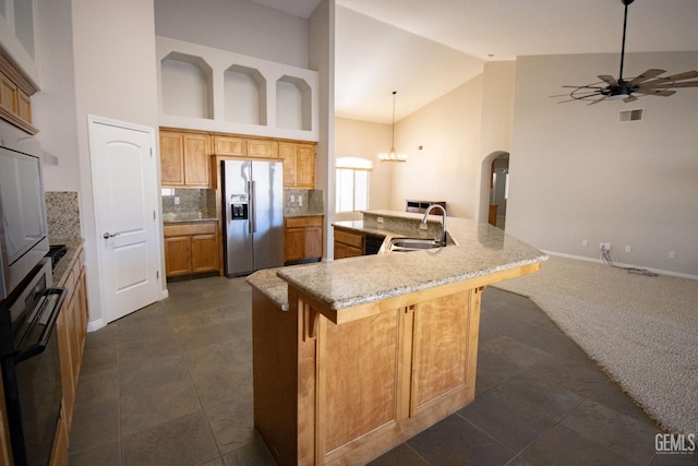 kitchen featuring stainless steel refrigerator with ice dispenser, tasteful backsplash, sink, hanging light fixtures, and oven