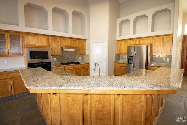 kitchen featuring a large island with sink, a towering ceiling, built in microwave, and high end refrigerator