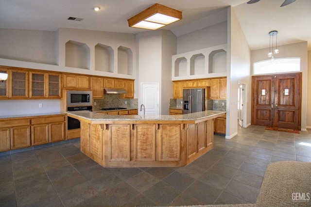 kitchen featuring high vaulted ceiling, decorative light fixtures, appliances with stainless steel finishes, and a kitchen island with sink