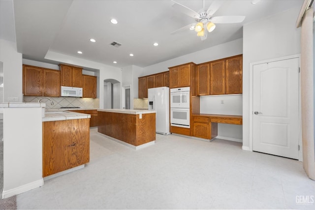 kitchen featuring a ceiling fan, tasteful backsplash, brown cabinets, and white appliances