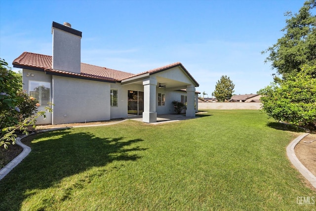 rear view of property featuring a tiled roof, ceiling fan, stucco siding, a lawn, and a chimney