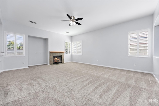 unfurnished living room with ceiling fan, carpet, a tile fireplace, and a healthy amount of sunlight