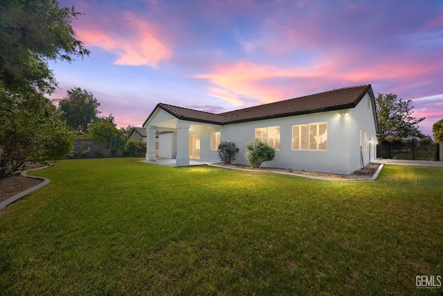 back of house at dusk featuring a yard, stucco siding, fence, and a tile roof