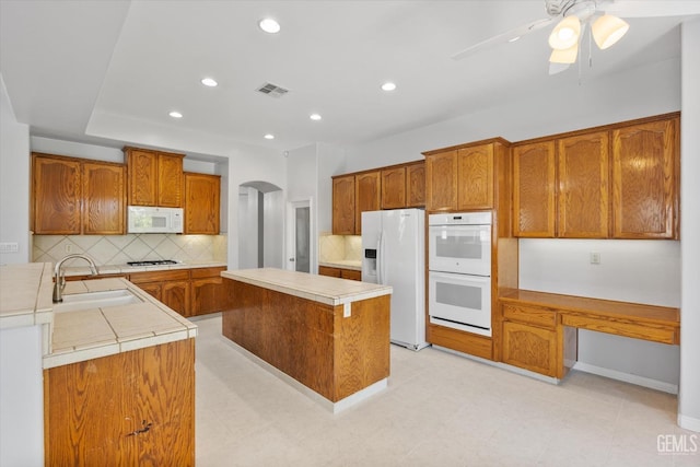 kitchen featuring white appliances, backsplash, visible vents, brown cabinets, and a sink