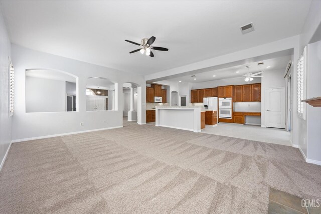 unfurnished living room with arched walkways, light carpet, baseboards, and a ceiling fan