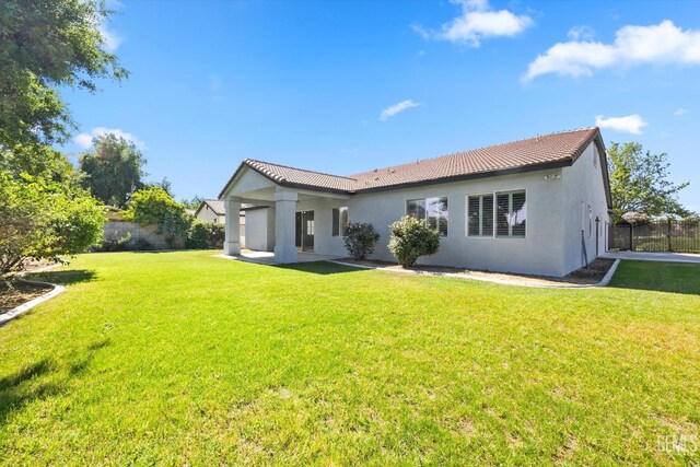 back of house featuring a yard, stucco siding, a tiled roof, and fence