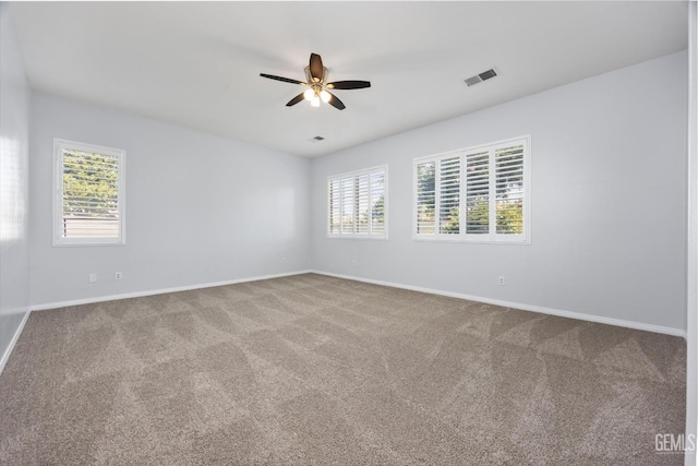 carpeted spare room with visible vents, baseboards, a ceiling fan, and a healthy amount of sunlight