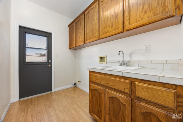laundry area featuring baseboards, light wood-type flooring, washer hookup, cabinet space, and a sink