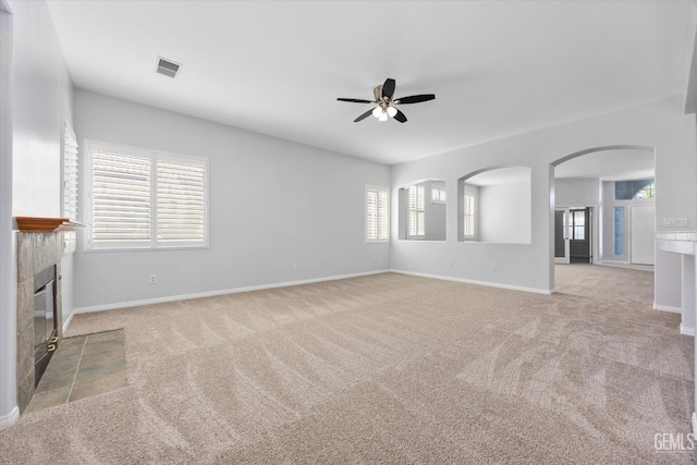 unfurnished living room with a tiled fireplace, visible vents, ceiling fan, and carpet flooring