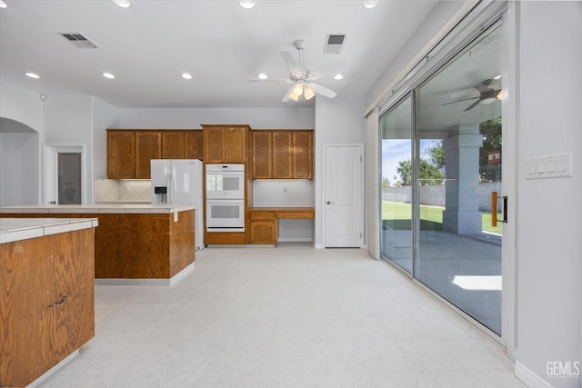 kitchen with brown cabinetry, a ceiling fan, visible vents, and white appliances