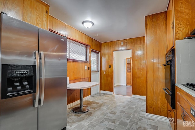 kitchen with black oven, white gas stovetop, stainless steel fridge with ice dispenser, and wood walls