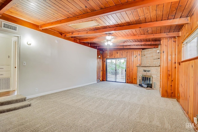 unfurnished living room with beam ceiling, a stone fireplace, carpet flooring, and wood walls