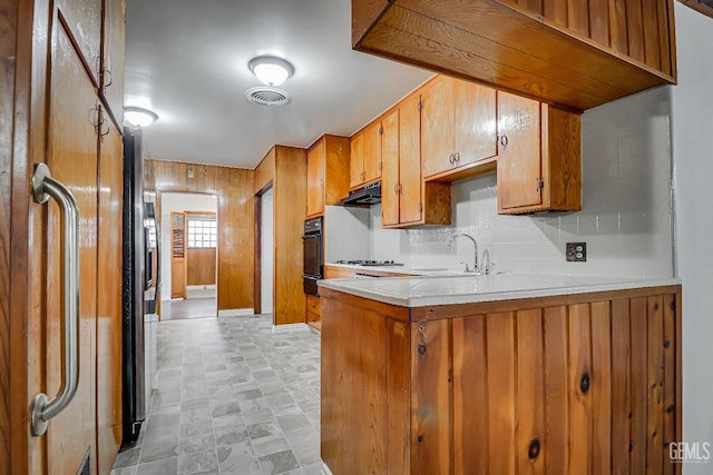 kitchen featuring sink, wood walls, kitchen peninsula, black oven, and decorative backsplash