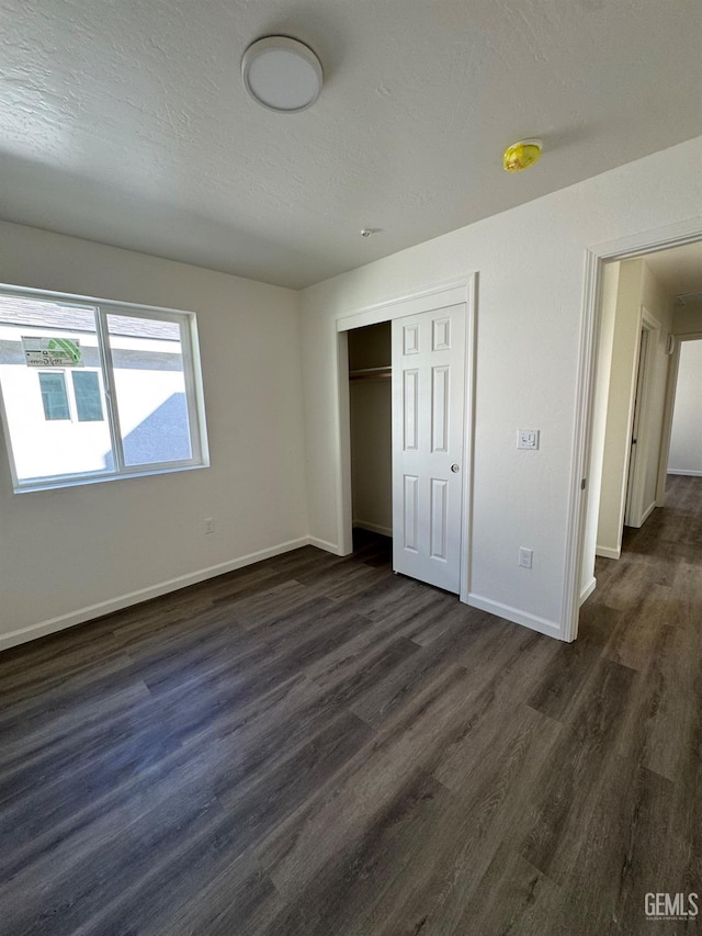 unfurnished bedroom with dark wood-type flooring, baseboards, a closet, and a textured ceiling