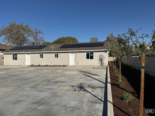 back of property with a fenced backyard, roof mounted solar panels, and stucco siding