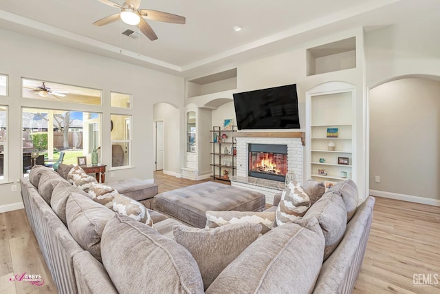 living room featuring a brick fireplace, built in shelves, ceiling fan, and light wood-type flooring