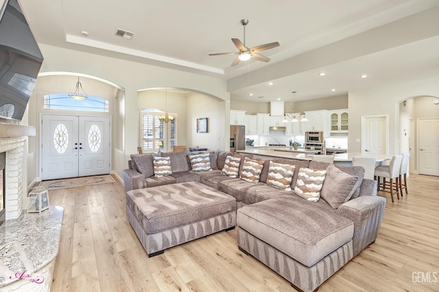 living room with a raised ceiling, sink, ceiling fan with notable chandelier, and light wood-type flooring