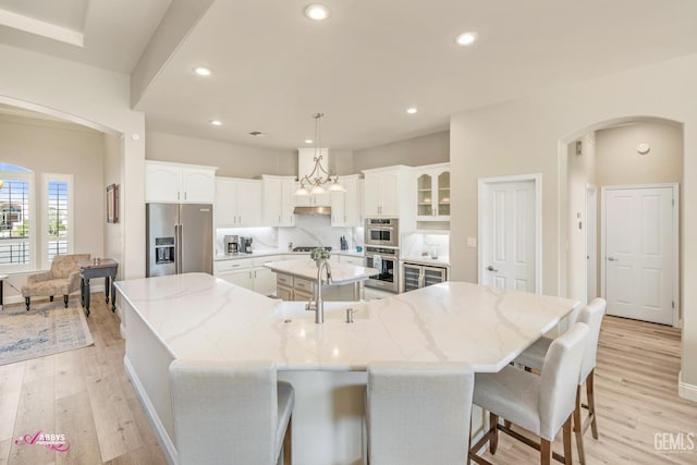 kitchen with white cabinetry, hanging light fixtures, stainless steel appliances, a large island, and light stone countertops