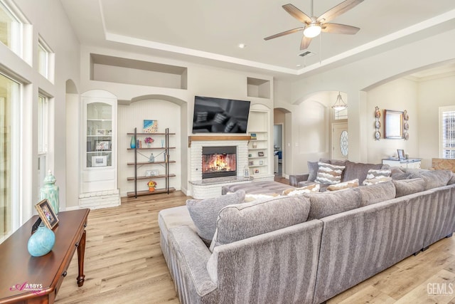 living room with a raised ceiling, built in features, a wealth of natural light, a fireplace, and light hardwood / wood-style floors