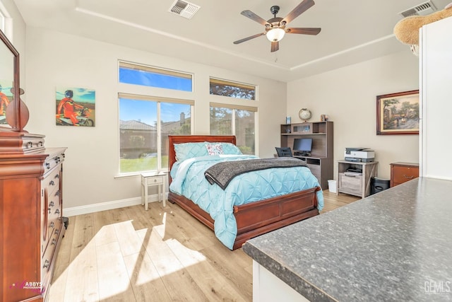 bedroom featuring a raised ceiling, ceiling fan, and light wood-type flooring