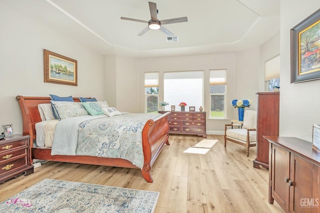 bedroom featuring ceiling fan, a tray ceiling, and light wood-type flooring