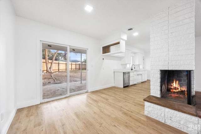 unfurnished living room featuring a fireplace, sink, and light wood-type flooring