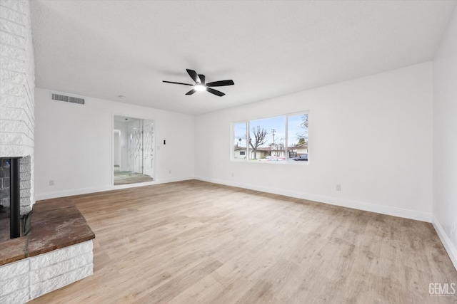 unfurnished living room with ceiling fan, light wood-type flooring, a textured ceiling, and a fireplace