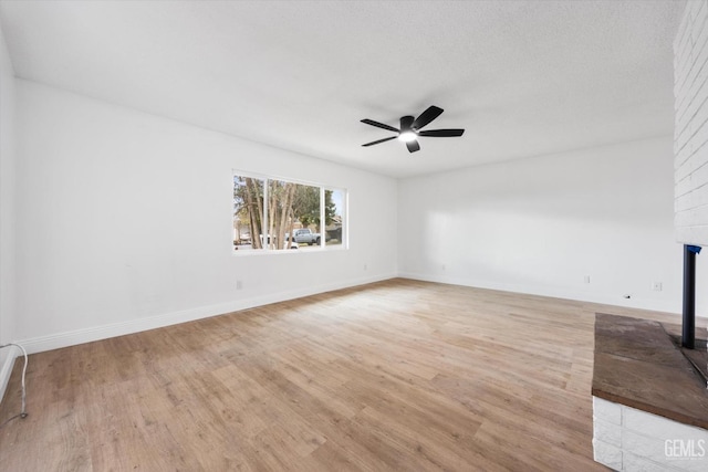 spare room featuring ceiling fan, a fireplace, light hardwood / wood-style flooring, and a textured ceiling