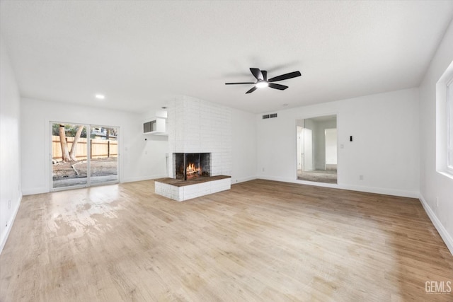 unfurnished living room with ceiling fan, a fireplace, light hardwood / wood-style flooring, and a textured ceiling